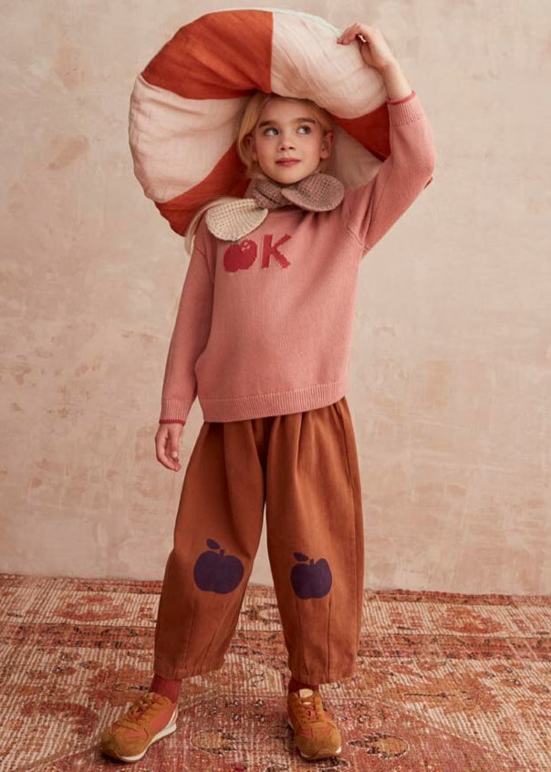 Child wearing a pink sweater with 'OK' and brown pants