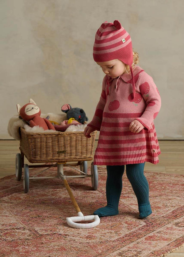 Child in a pink cotton dress with apple pattern and striped hat 
