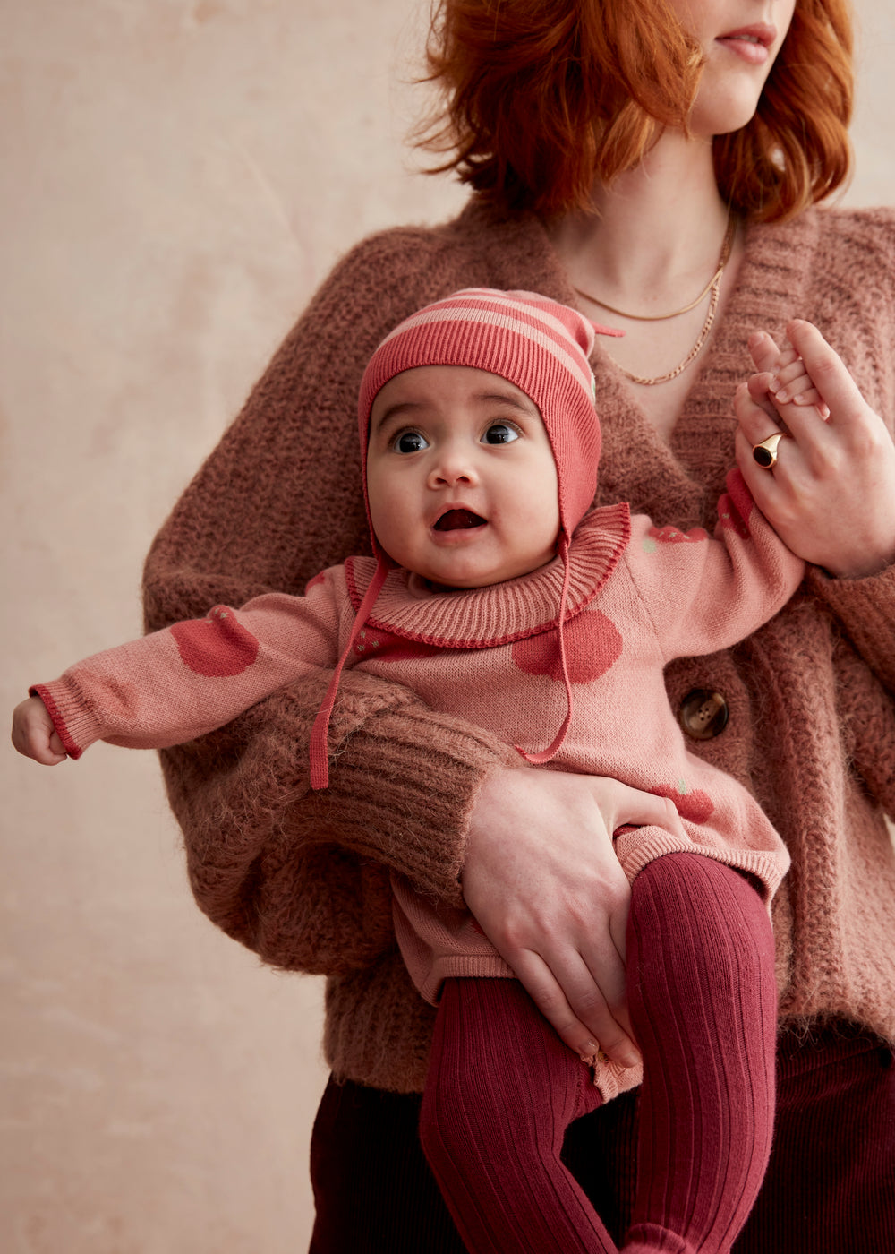 baby dressed in pink and red romper with apple design and red and pink striped hat
