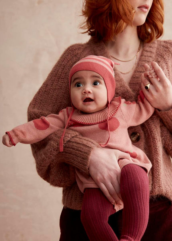 Baby in pink cotton romper with apple patterns and red tights