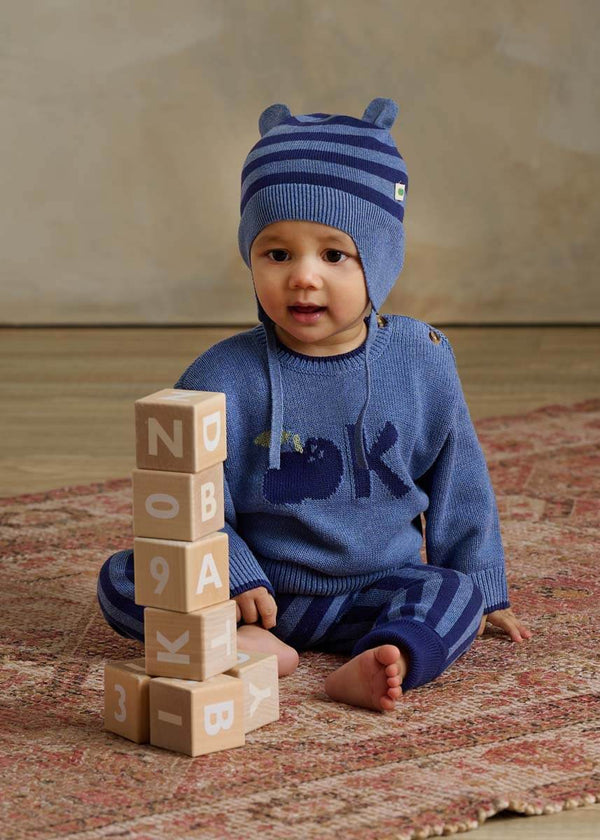 Baby wearing a blue cotton sweater with an apple design and striped hat