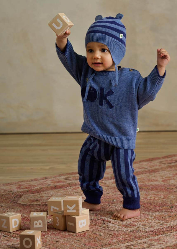 Child in a blue cotton sweater with an apple design and striped cotton trousers