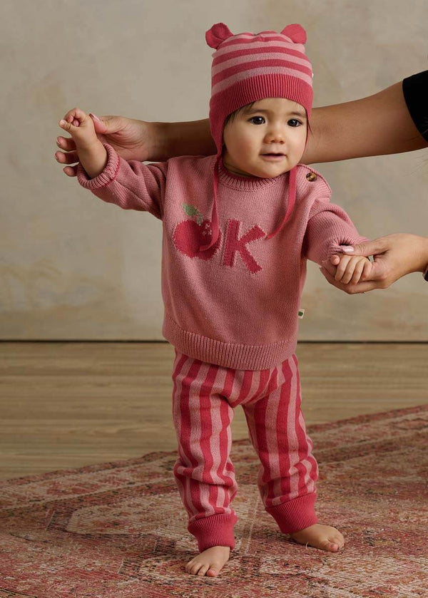 Baby in pink cotton sweater and trouser set with matching hat 