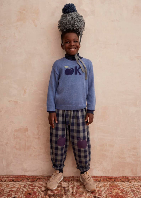 Child wearing a blue sweater with a logo and blue plaid pants with purple apple knee patches