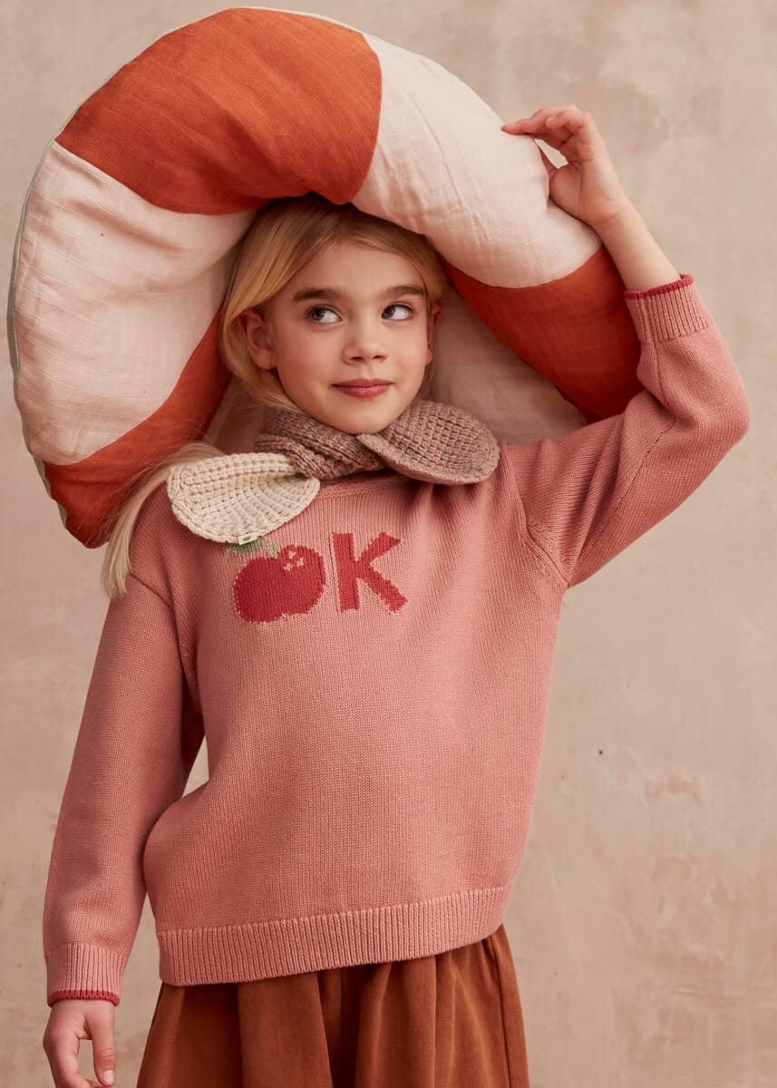 Child wearing a pink sweater with 'OK' and a knitted cream and pink scarf