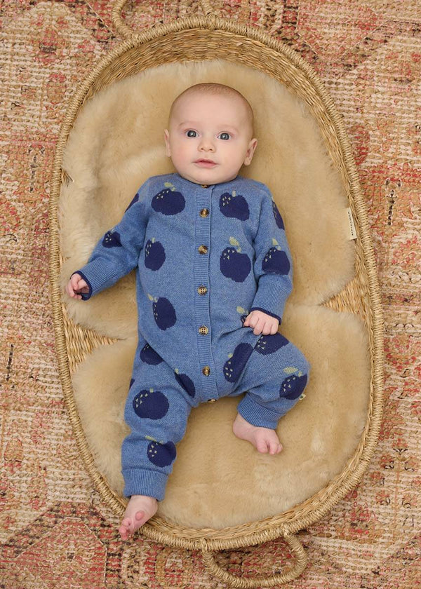 Baby in a blue cotton playsuit with apple patterns 