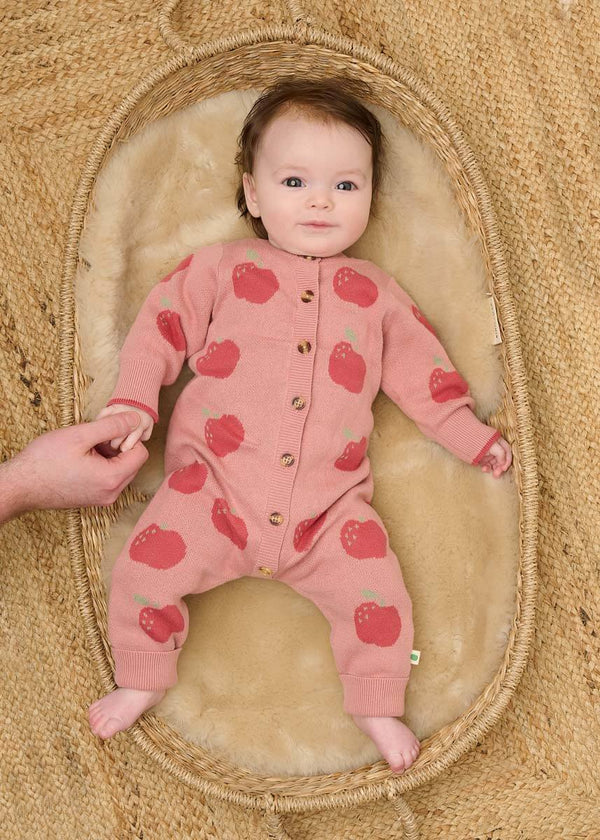 Baby in a pink cotton playsuit with red apple pattern 
