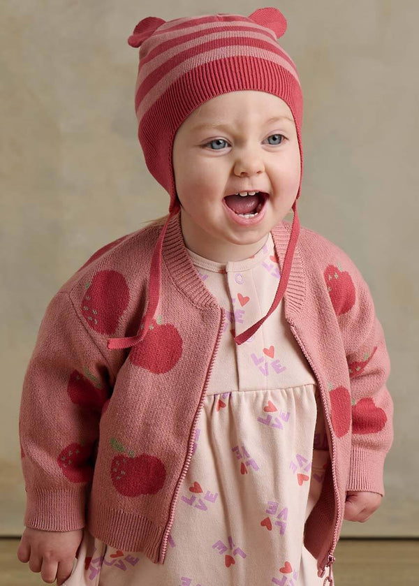 Child wearing a pink cotton cardigan with apple patterns and a matching hat 