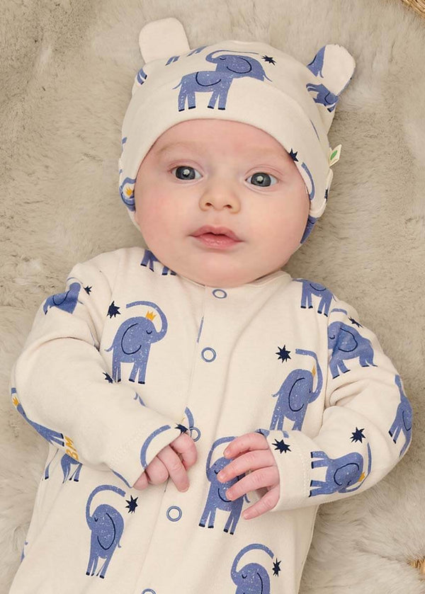 Baby wearing a white cotton onesie with blue elephant patterns and a matching hat 