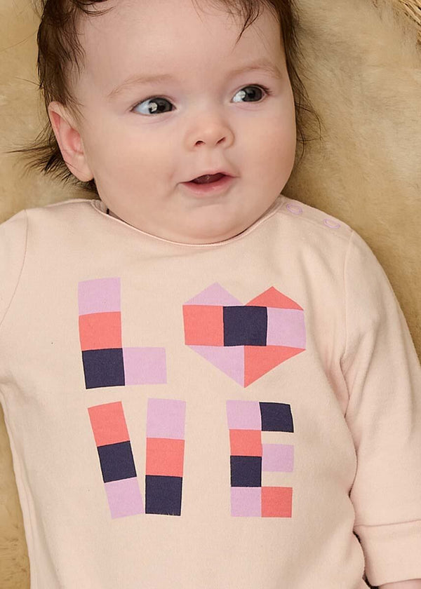Baby wearing a pink cotton playsuit with colorful geometric patterns 