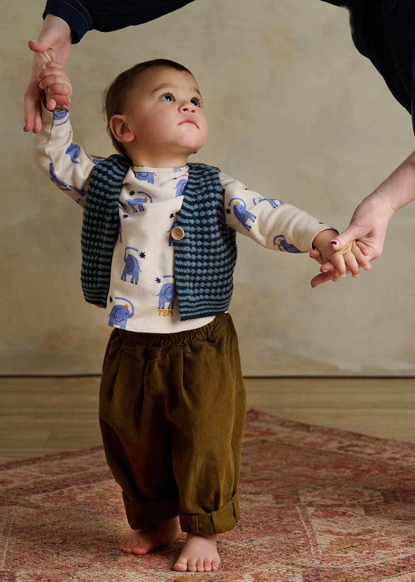 Child wearing a patterned shirt, vest, and green harem pants 