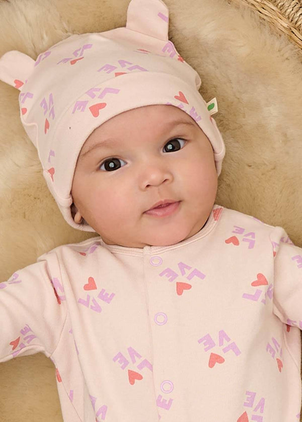 Baby wearing a pink outfit with heart patterns and a matching pink cotton hat.