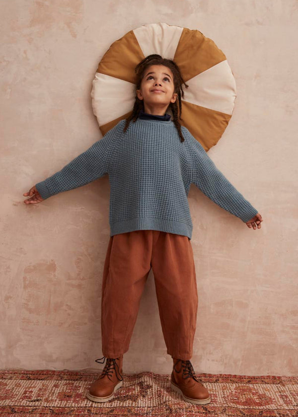 Child wearing a blue knit sweater and brown pants 