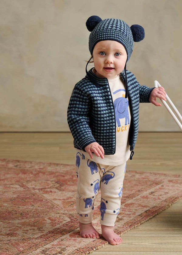 Child wearing a blue knit hat and jacket with blue cotton elephant-patterned leggings 