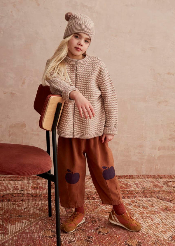 Child wearing a knit beige sweater and brown pants with purple accents, 