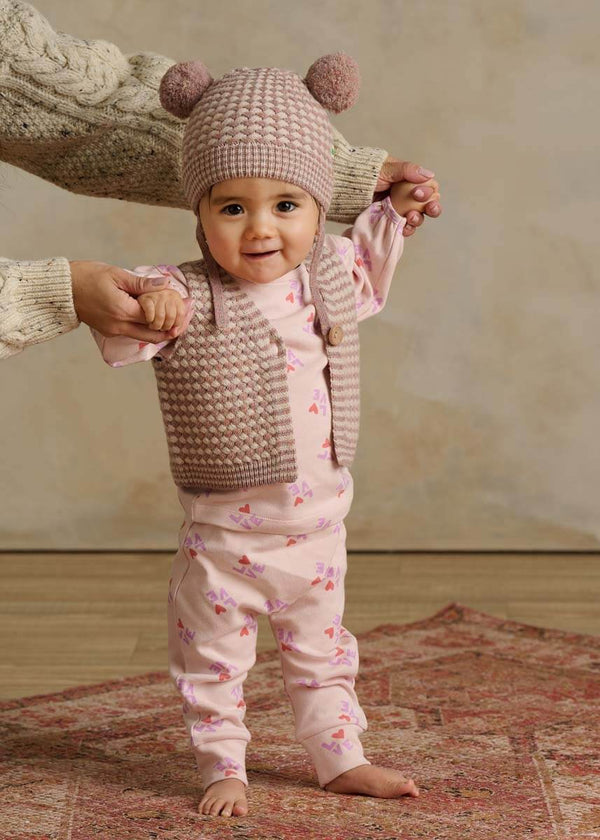 Baby in pink cotton outfit with a heart pattern with knitted hat and vest 